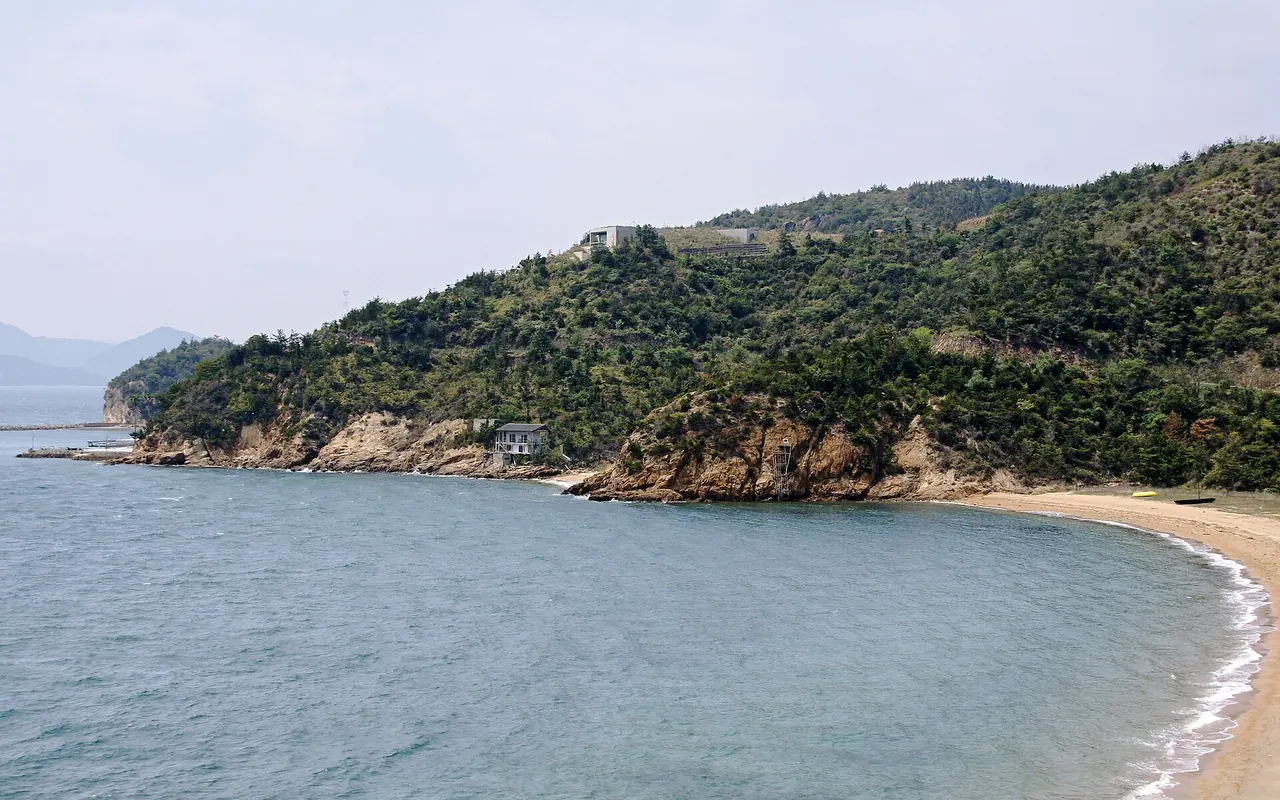 A sandy bay and a wooded headland on the coast of Naoshima below the museum