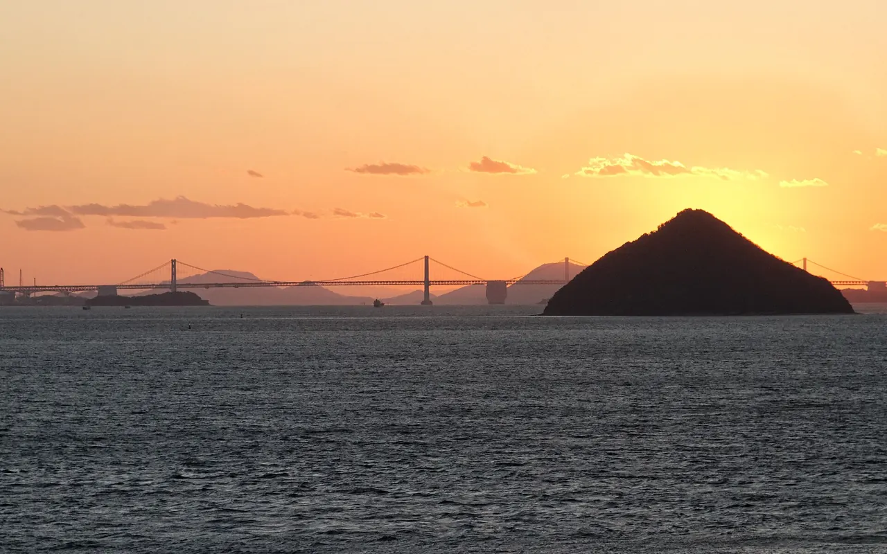 Sunset over the Seto Inland Sea with a conical island and a long suspension bridge on the horizon