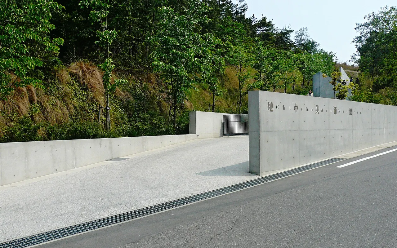 A long concrete wall by the road bearing the name of the Chichu Art Museum, with trees behind